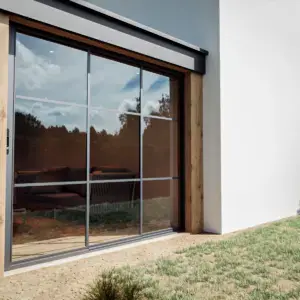 Steellook glazen schuifwand met 3 rails met witte muur ernaast en nette tuin ervoor