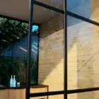Steellook glazen schuifwand met 3 rails met aanrecht binnen en houten muur ernaast