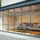 Steellook glazen schuifwand met 6 rails van vooraf, met lage tafel en bank ingericht en tuin met padje van vooraf